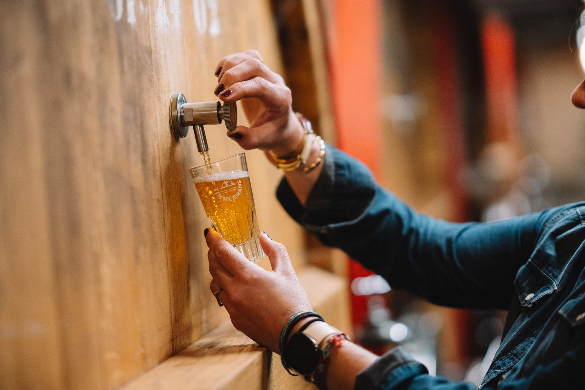Iemand tapt een glas Timmermans bier rechtstreeks uit een groot houten vat
