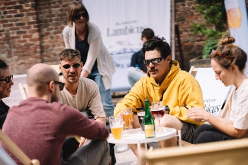 Een groep mensen zit buiten op een terras in strandstoelen te praten en te drinken bij een tafeltje met bier