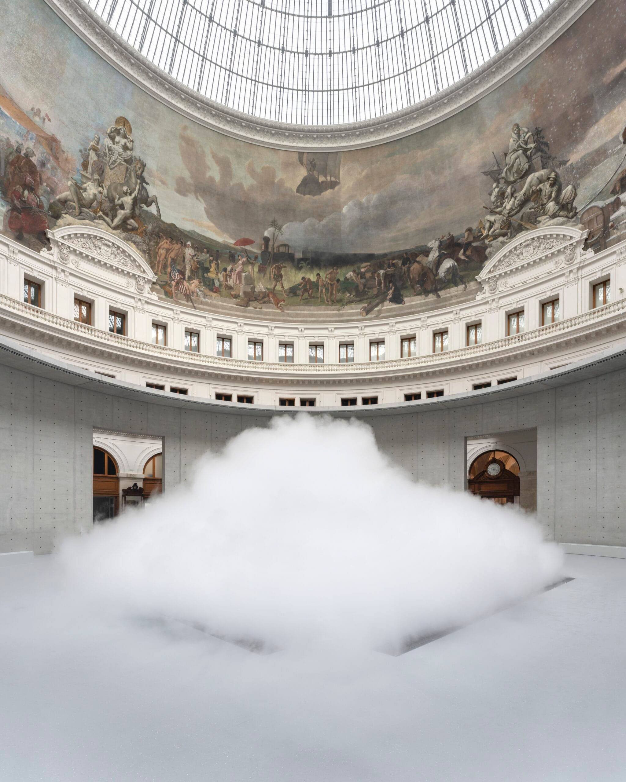 Een grote witte mistwolk in het midden van de ronde, betonnen zaal van de Bourse de Commerce onder een koepel met fresco's