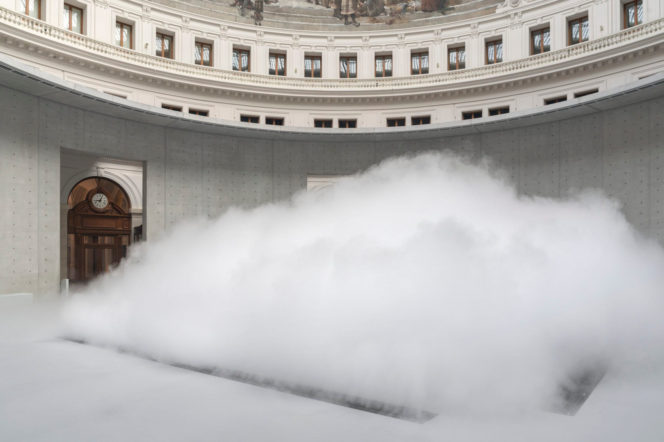 Een grote witte mistwolk vult de centrale ronde hal van een museum met betonnen muren en een klassieke koepel