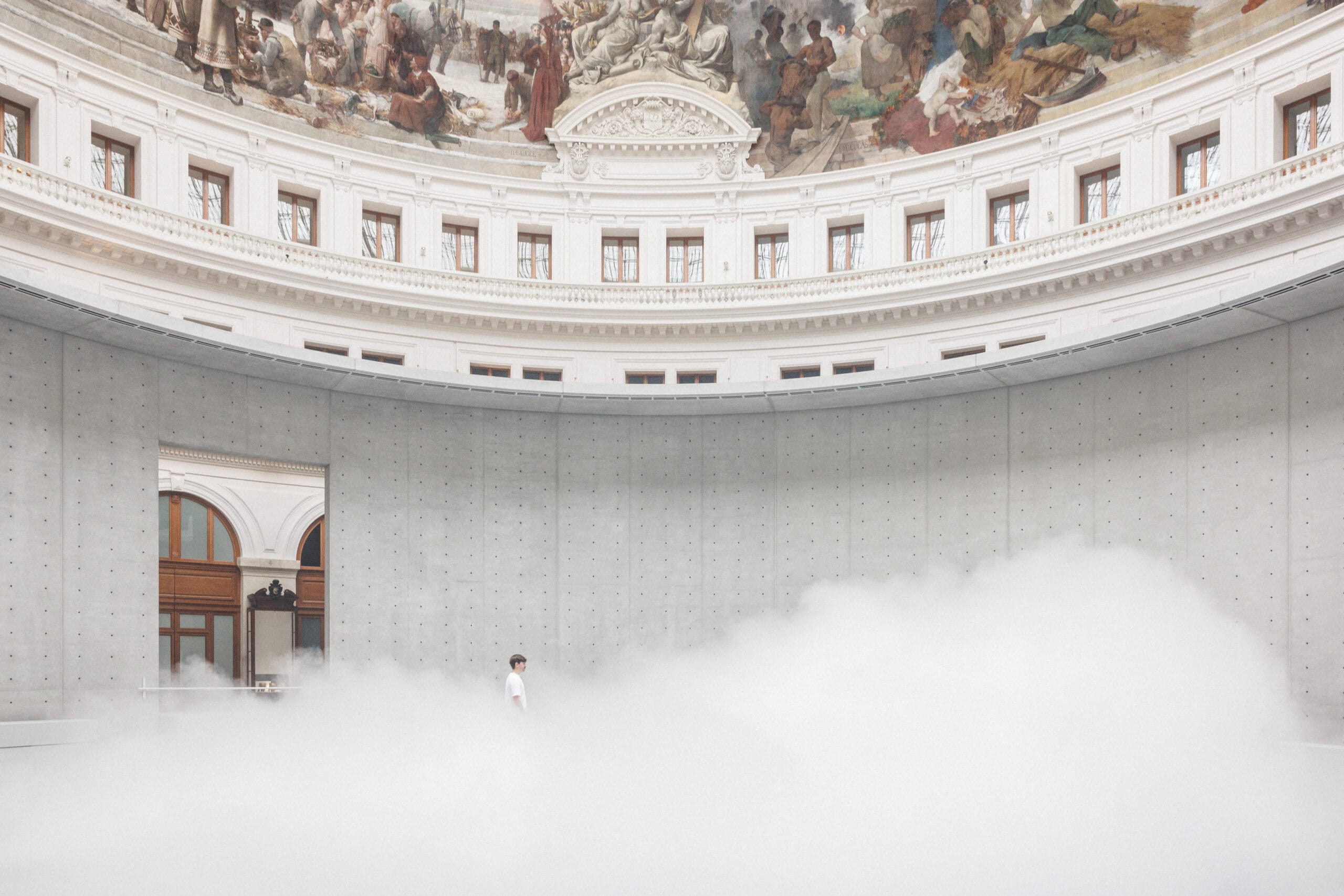 Een persoon loopt door een dikke laag mist in de moderne betonnen rotonde van de Bourse de Commerce in Parijs