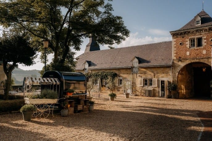 Binnenplaats van een het historische landgoed Château Neercanne met een stenen bijgebouw, een poortgebouw en een decoratieve bloemenkar, restaurant L'Auberge