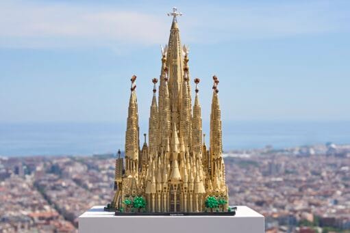 Een gedetailleerd LEGO-model van de Sagrada Família op een witte sokkel met de stad Barcelona op de achtergrond