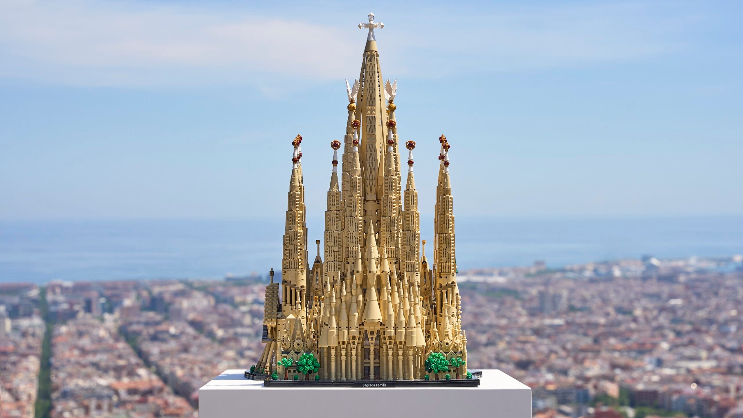 Een gedetailleerd LEGO-model van de Sagrada Família op een witte sokkel met de stad Barcelona op de achtergrond