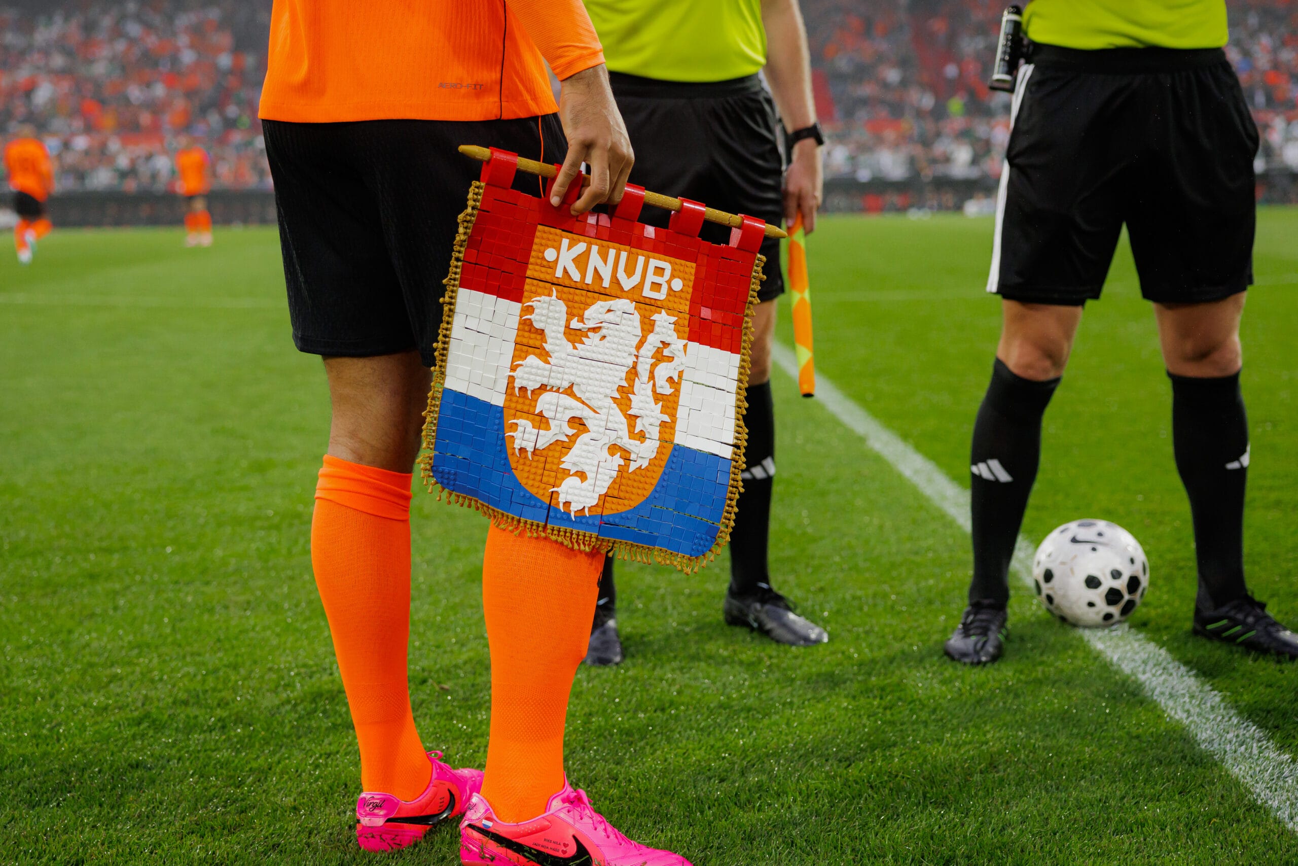 Een voetballer houdt een KNVB-vaantje van bouwstenen vast op het veld voor de aftrap