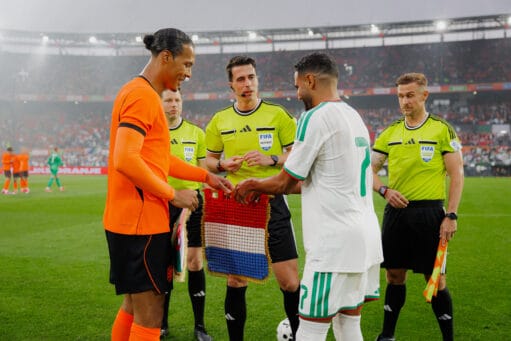 Virgil van Dijk en de aanvoerder van Algerije wisselen vaantjes uit voor de wedstrijd onder toezicht van de scheidsrechters