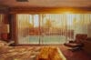 Schilderij van Yigal Ozeri van een slaapkamer in retrostijl met uitzicht op een zwembad door een glazen schuifpui met lamellen