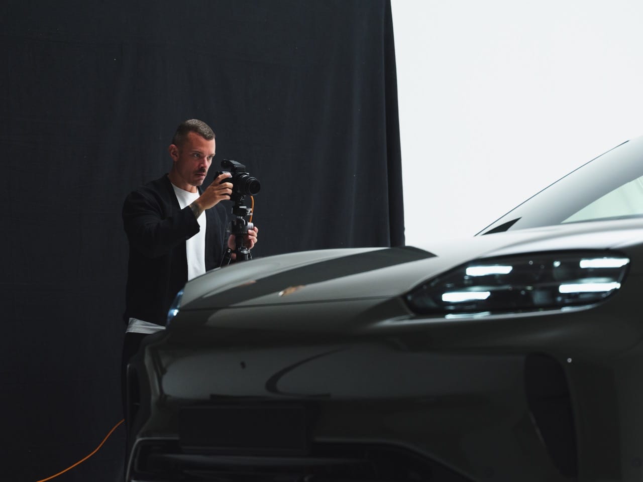 Een fotograaf maakt in een studio opnames van de voorkant van een moderne auto tegen een zwarte achtergrond