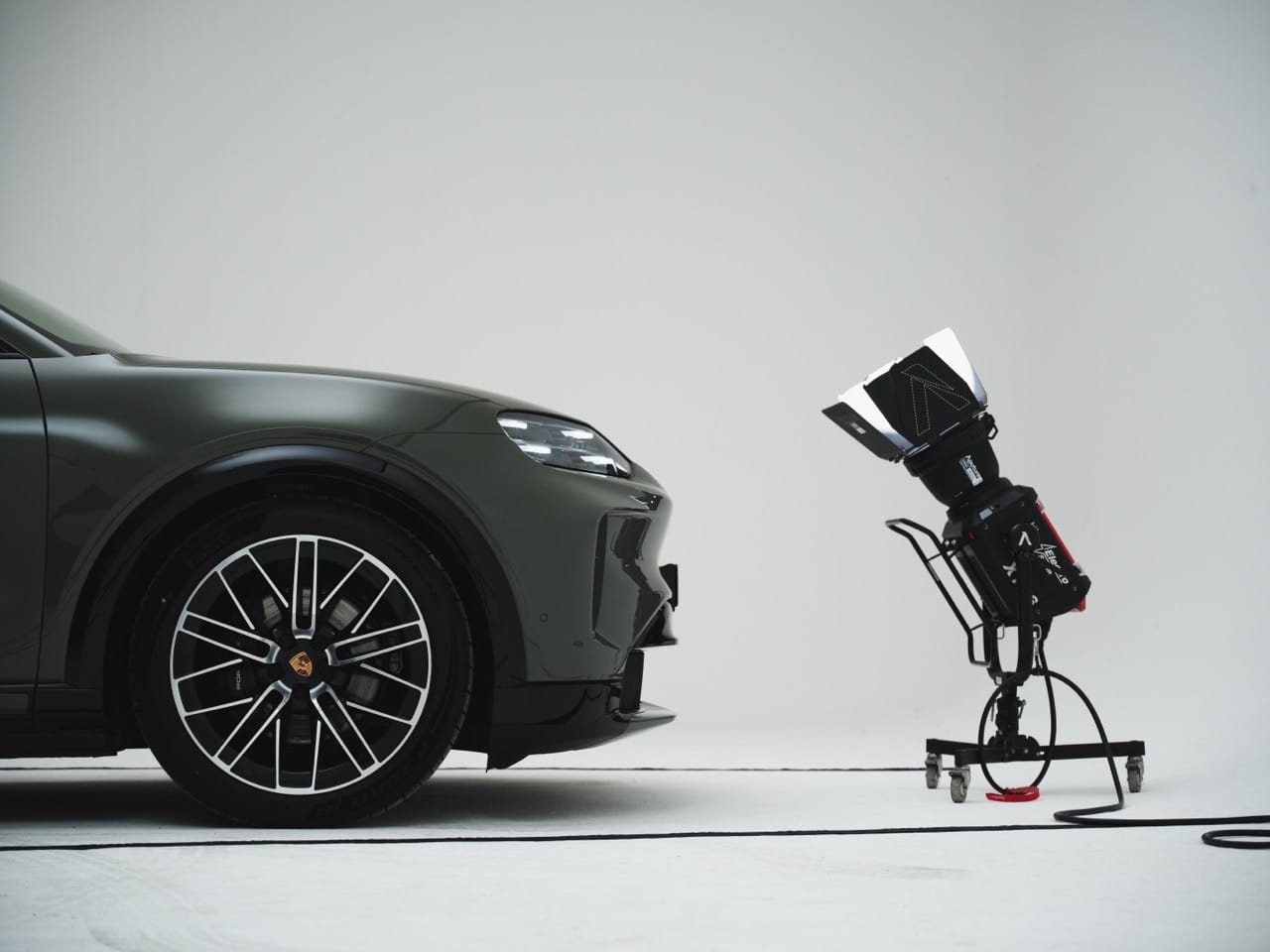 Zijaanzicht van de voorkant van een olijfgroene Porsche Macan in een fotostudio met een studiolamp