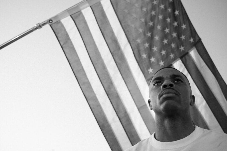 Zwart-wit portret van een jonge man die omhoog kijkt met de Amerikaanse vlag op de achtergrond