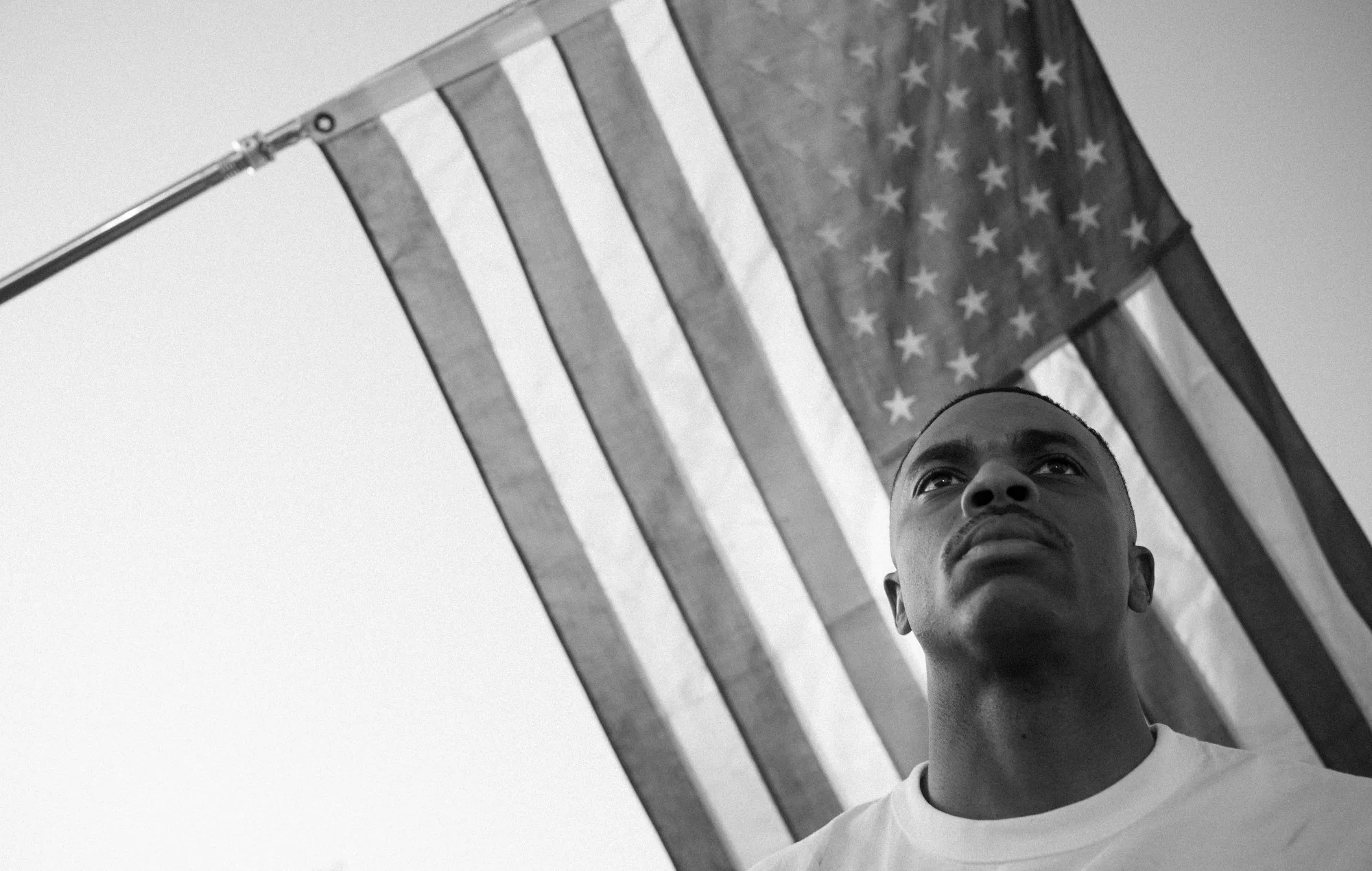 Zwart-wit portret van een jonge man die omhoog kijkt met de Amerikaanse vlag op de achtergrond