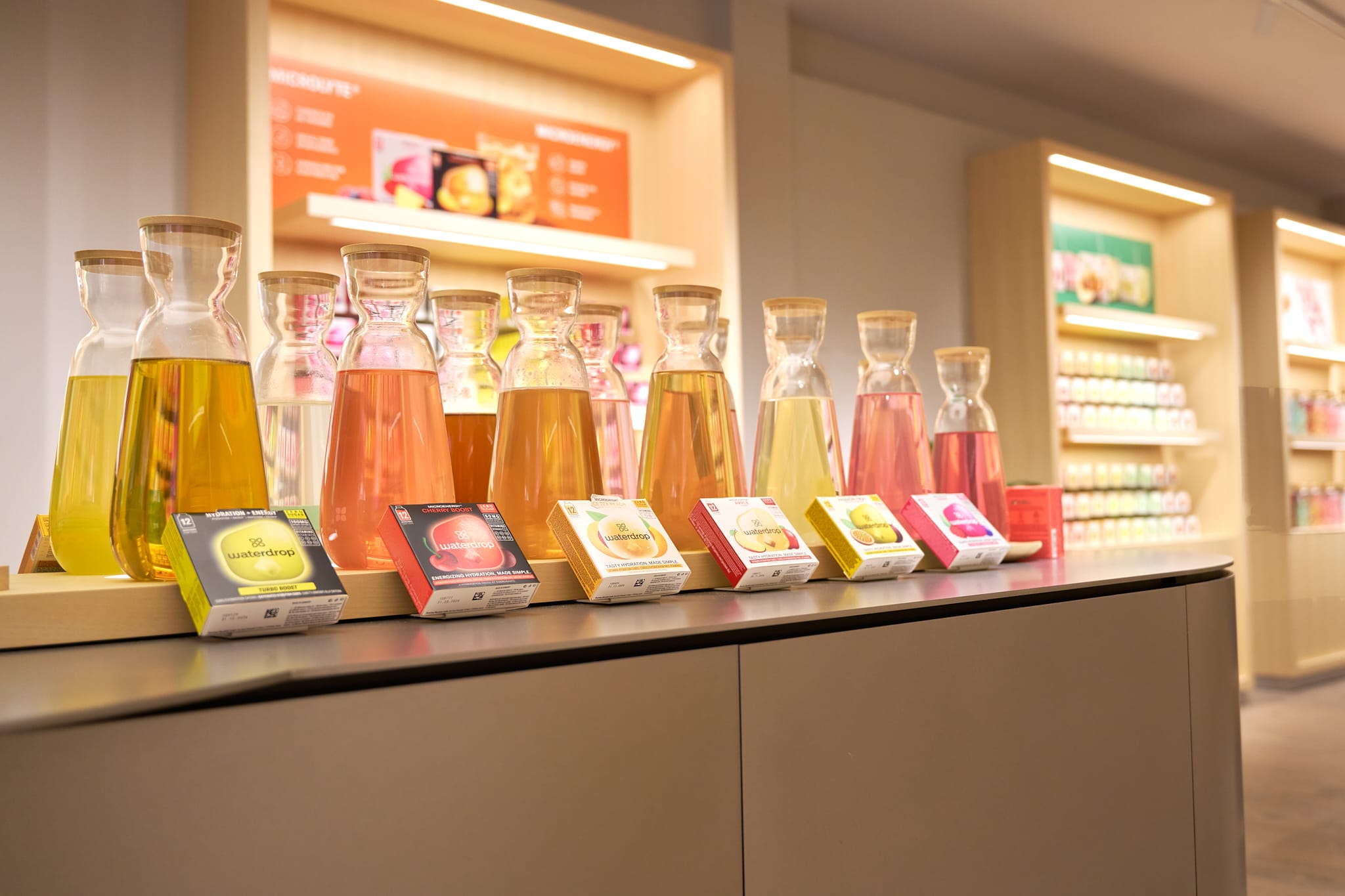 Glazen karaffen met kleurrijke dranken en bijbehorende Waterdrop-verpakkingen op een toonbank in een winkel
