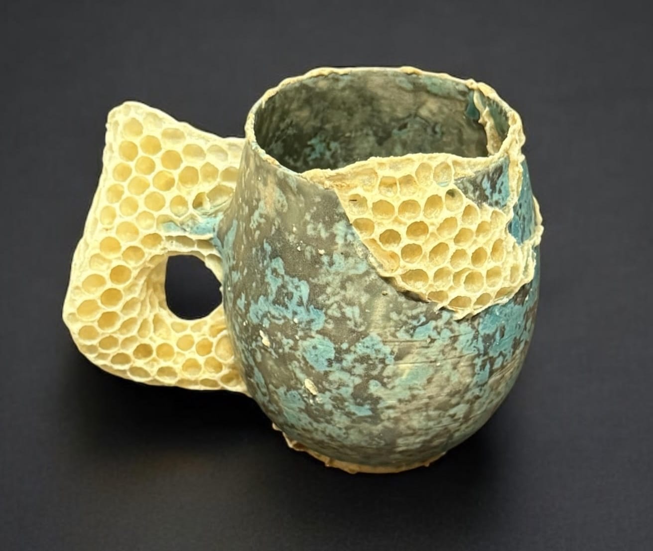Een turquoise, keramieken mok met een handvat en details van gele bijenraatstructuur