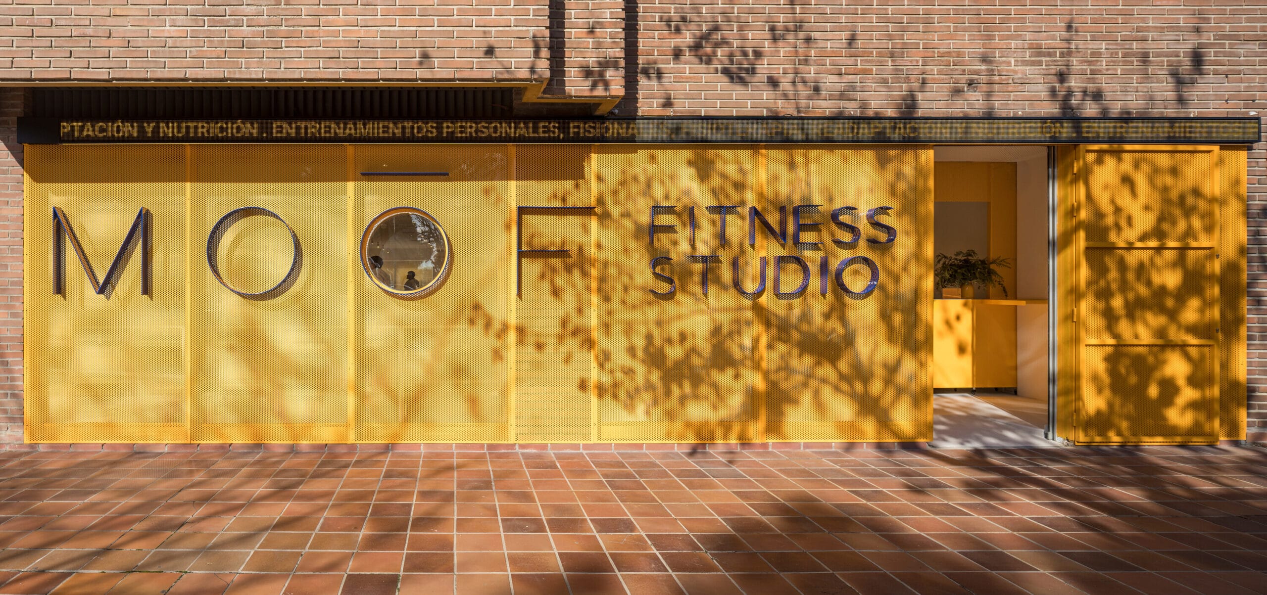 Gevel van MOOF Fitness Studio met een opvallende gele geperforeerde wand en blauwe belettering