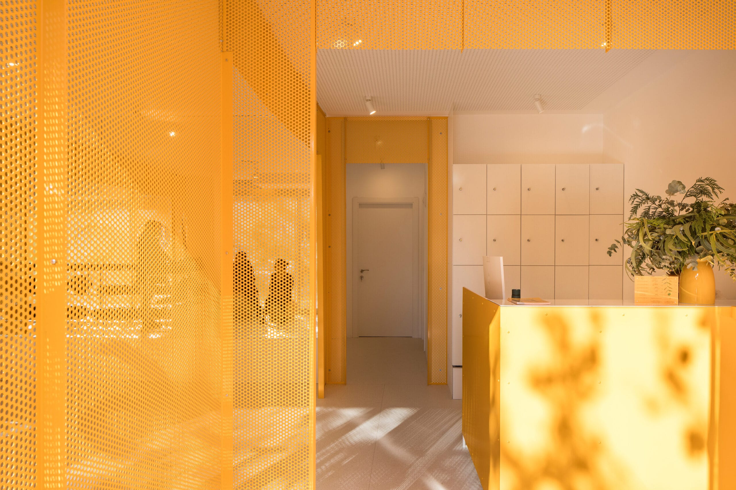 Modern interieur van een ontvangstruimte met een gele balie, witte kluisjes en opvallende gele geperforeerde wanden