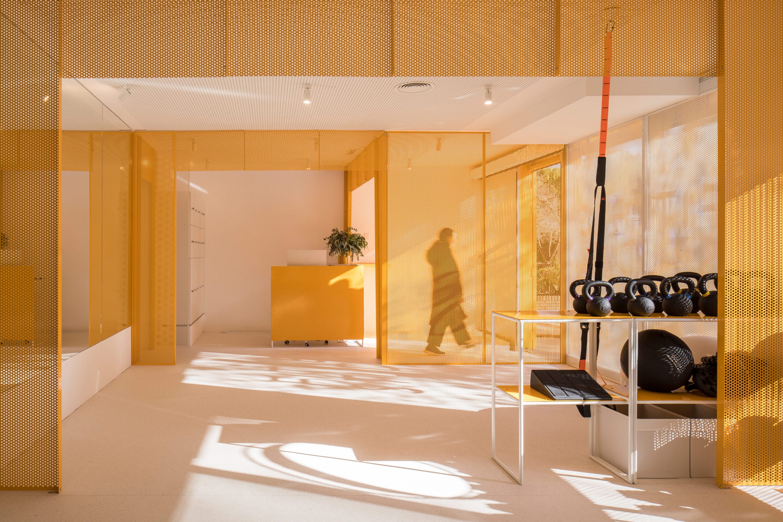 Modern interieur van een sportschool met gele geperforeerde wanden, een balie en fitnessattributen zoals kettlebells
