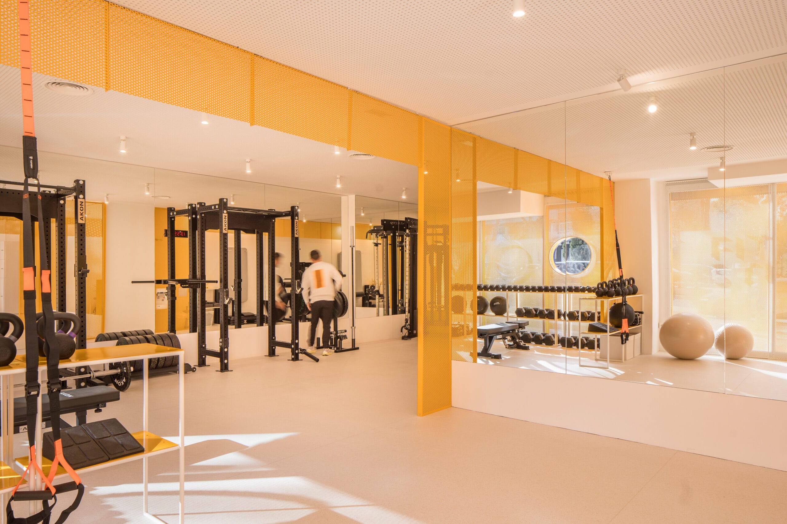 Moderne fitnessruimte met gele accenten, krachtstations, spiegels en een rek met dumbbells