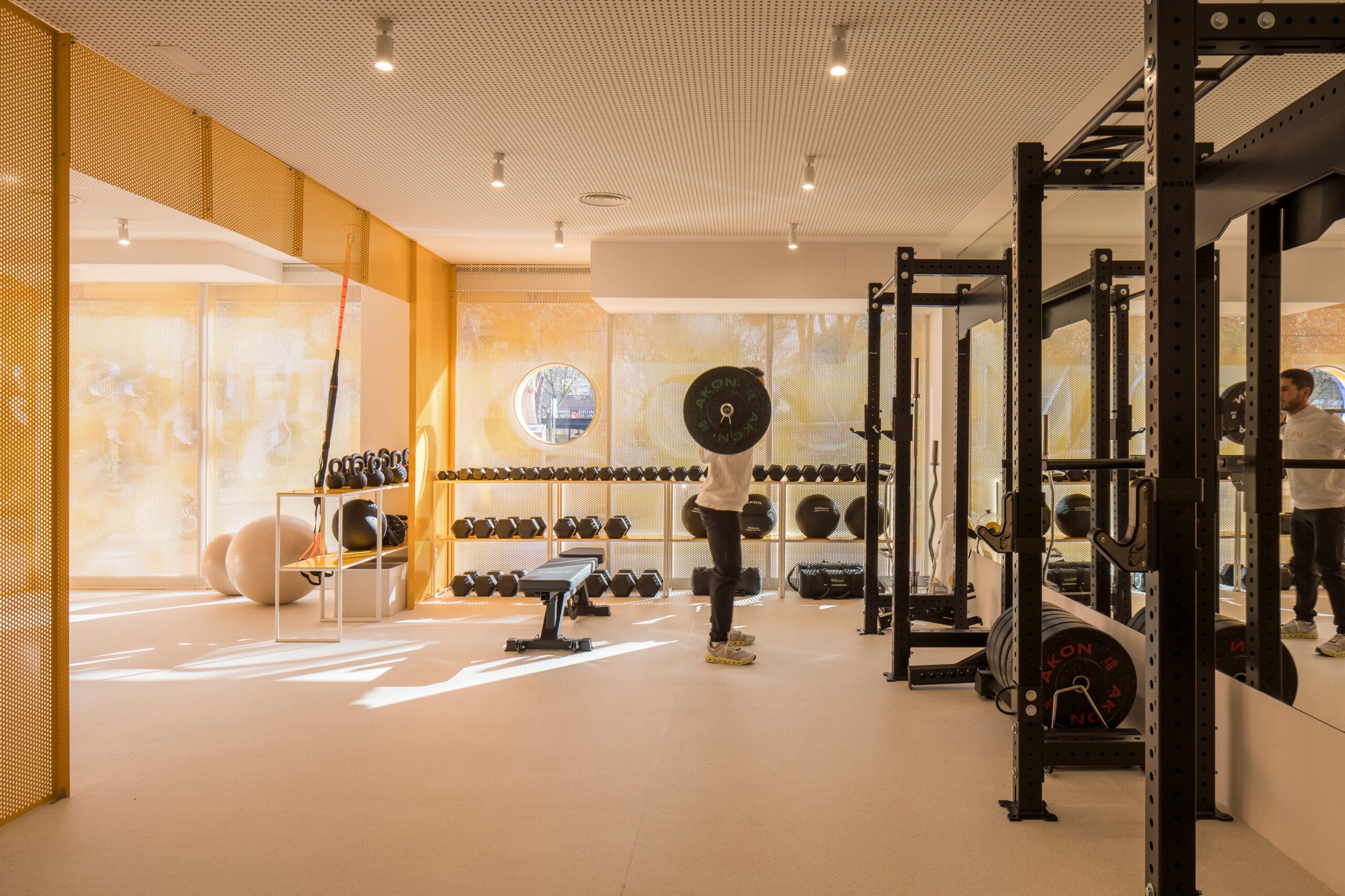 Een man traint met een halterstang in een moderne sportschool met gele geperforeerde wanden en diverse fitnessapparatuur