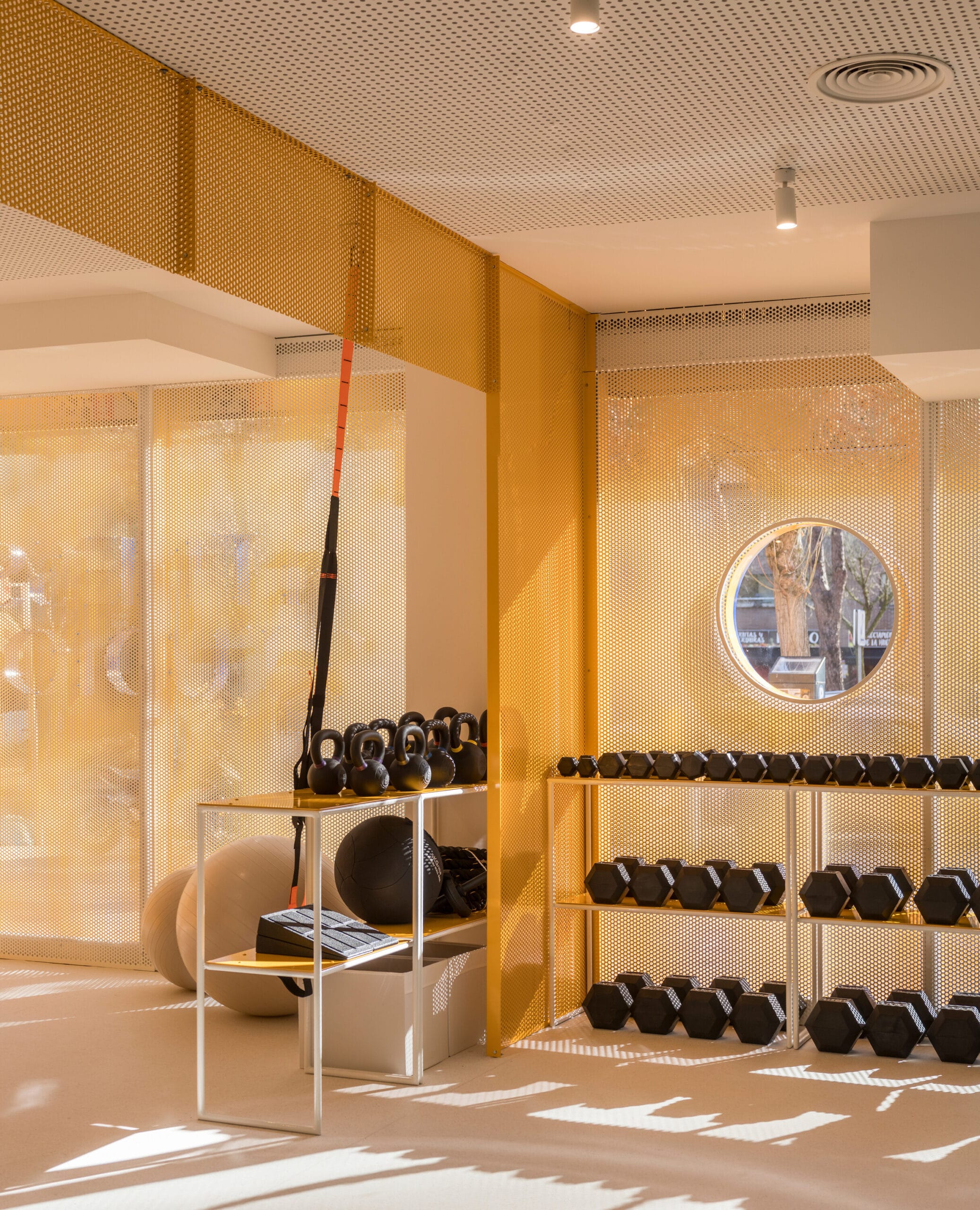 Moderne fitnessruimte met gele geperforeerde wanden, rekken met dumbbells, kettlebells en fitnessballen