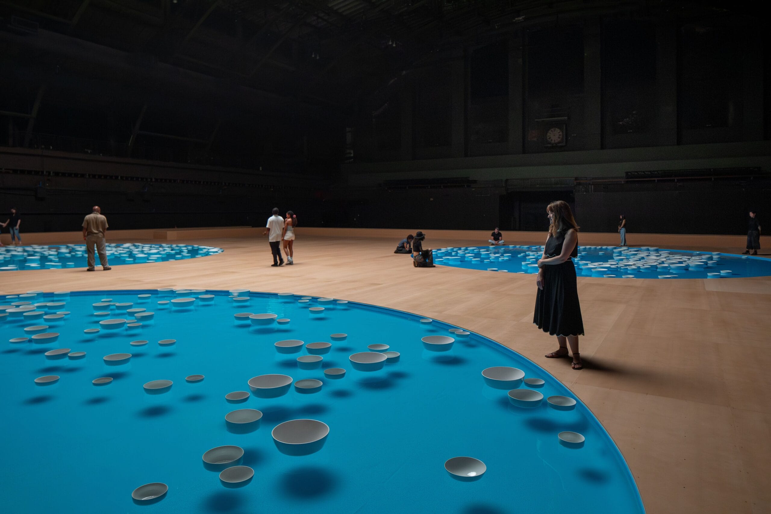Bezoekers in de Park Avenue Armory bij ronde blauwe waterbassins waarin witte porseleinen kommen drijven