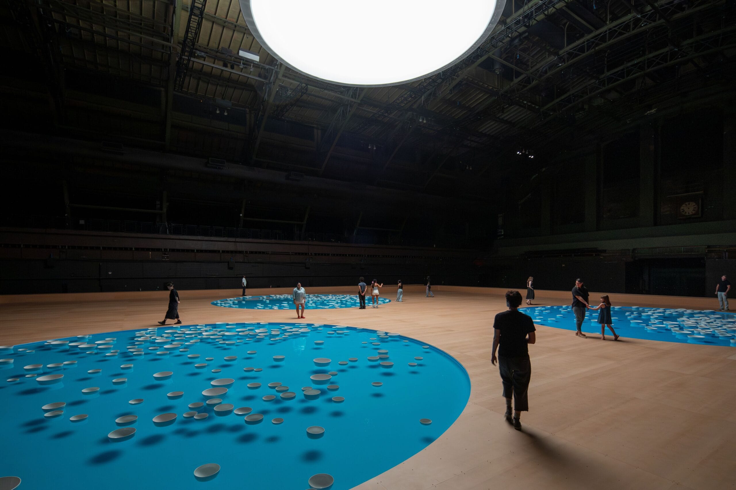 Overzicht van de installatie clinamen in de Park Avenue Armory, met bezoekers rondom drie grote blauwe waterbassins