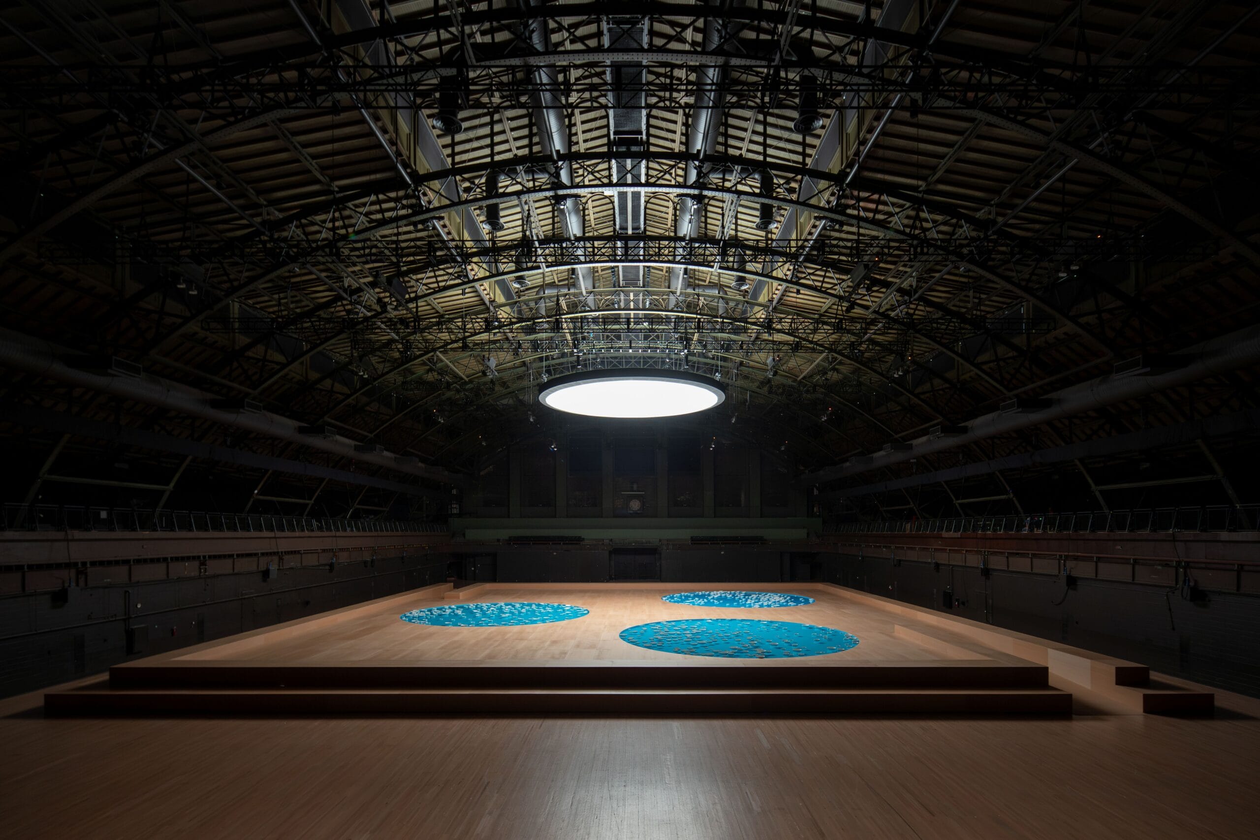 Overzicht van de installatie clinamen in de enorme, donkere Drill Hall met drie blauwe ronde waterbassins