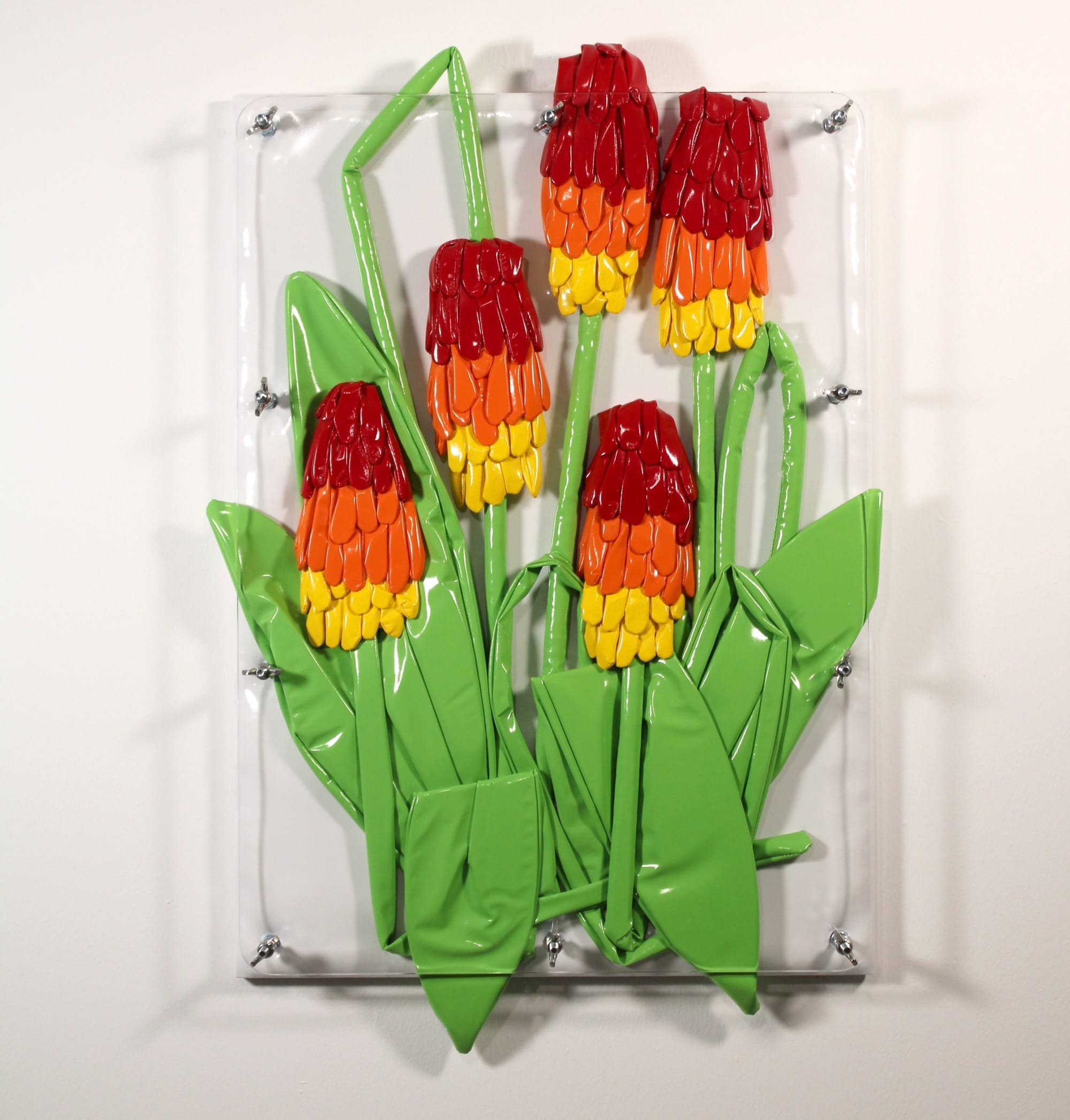 Wandsculptuur van vijf rood-geel-oranje bloemen met groene bladeren, gemaakt van glanzend gevouwen materiaal