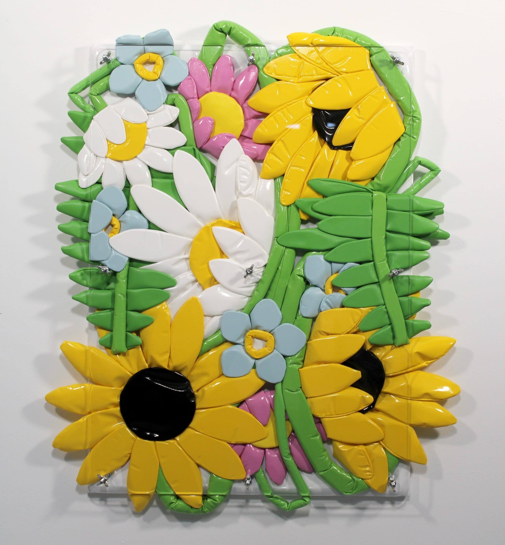 Kleurrijk reliëfkunstwerk van opgeblazen plastic bloemen, waaronder zonnebloemen en madelieven, gemonteerd op een paneel