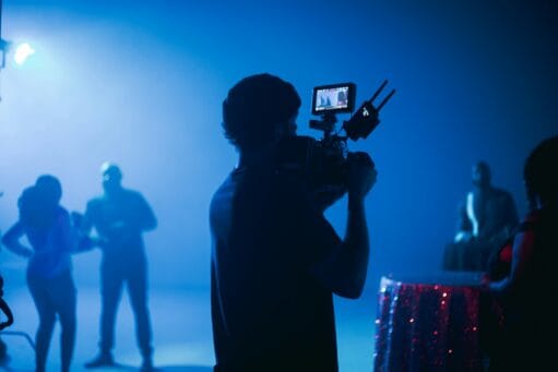 Een cameraman filmt dansende mensen in een studio met blauwe belichting