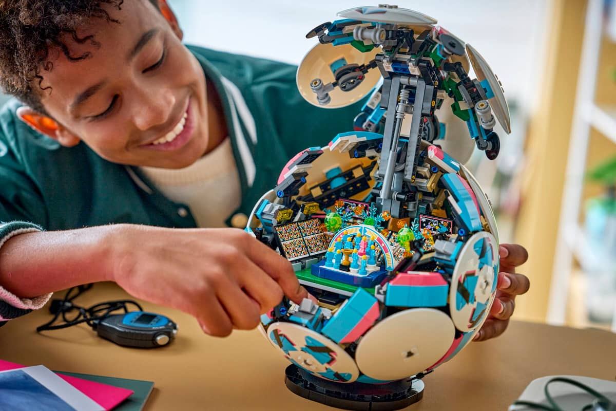 Een lachende jongen speelt met een opengeklapte, bolvormige LEGO-set die van binnen een gedetailleerd futuristisch stadion toont