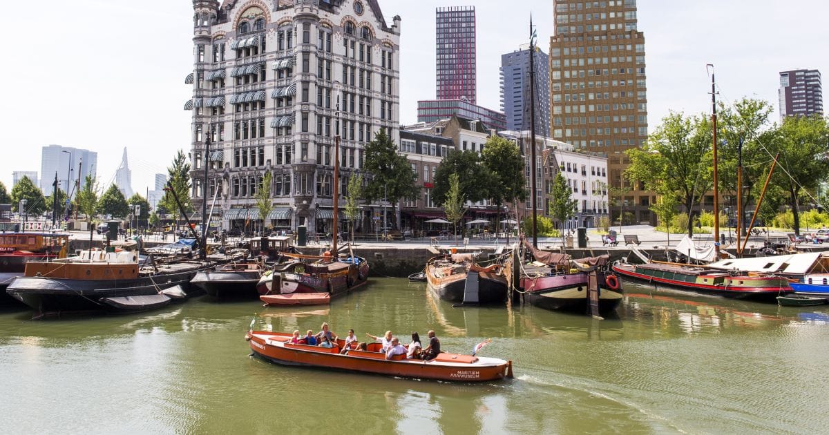 Een oranje rondvaartboot van het Maritiem Museum met passagiers vaart in de Leuvehaven in Rotterdam, met het Witte Huis