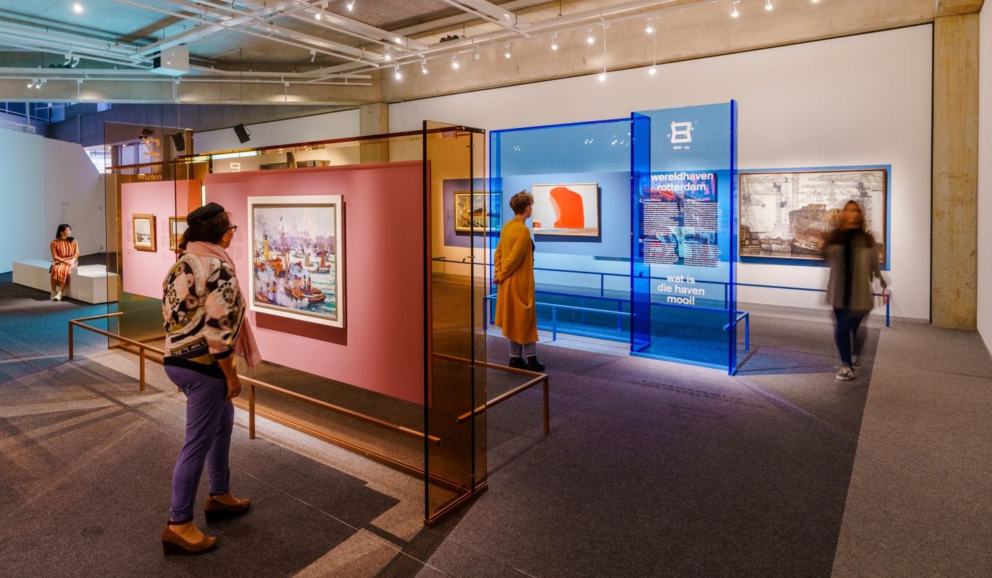 Bezoekers bekijken schilderijen van de Rotterdamse haven in een modern ingerichte museumzaal met kleurrijke panelen
