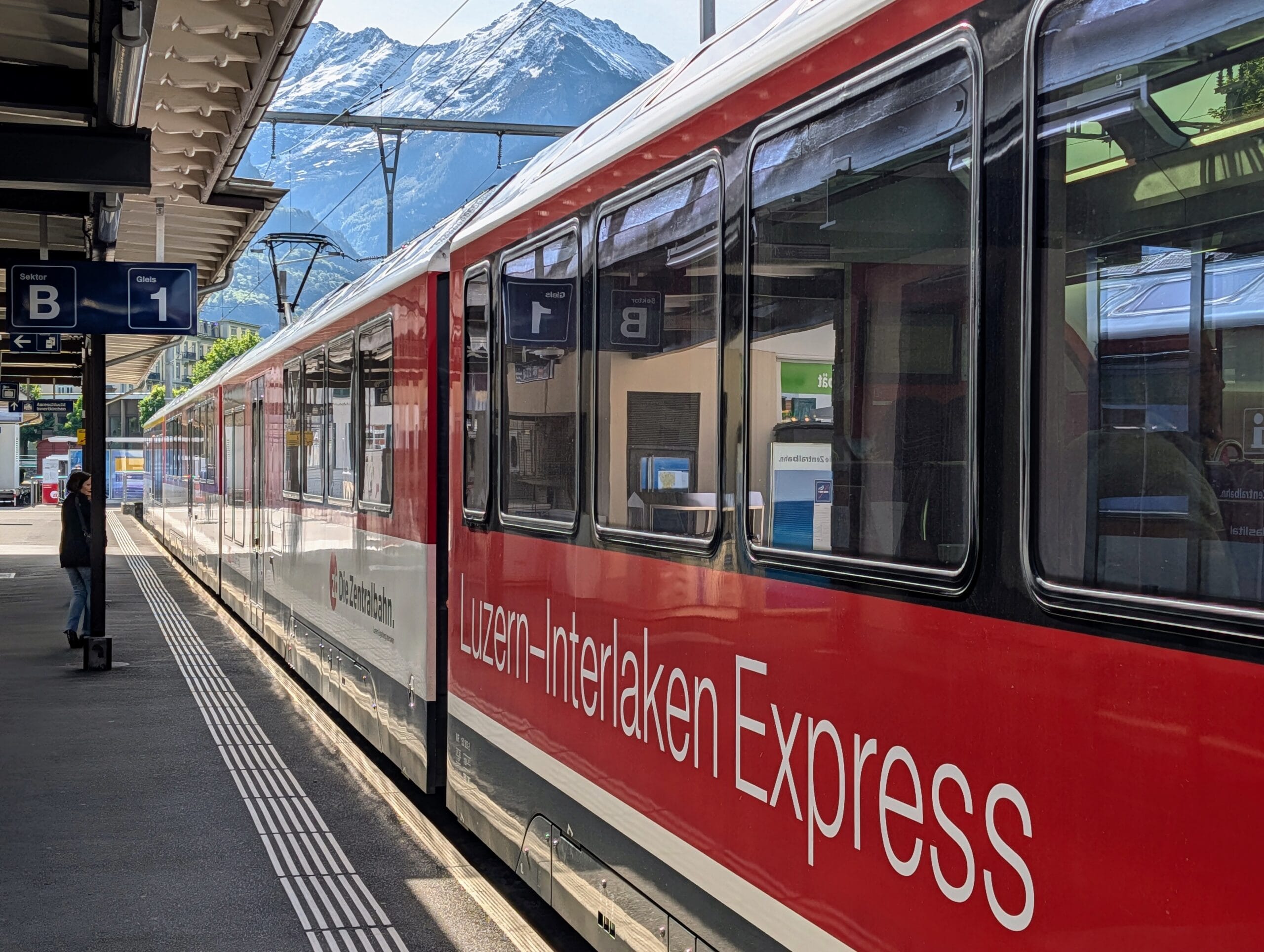 De rood-witte Luzern-Interlaken Express staat langs het perron met op de achtergrond besneeuwde bergtoppen