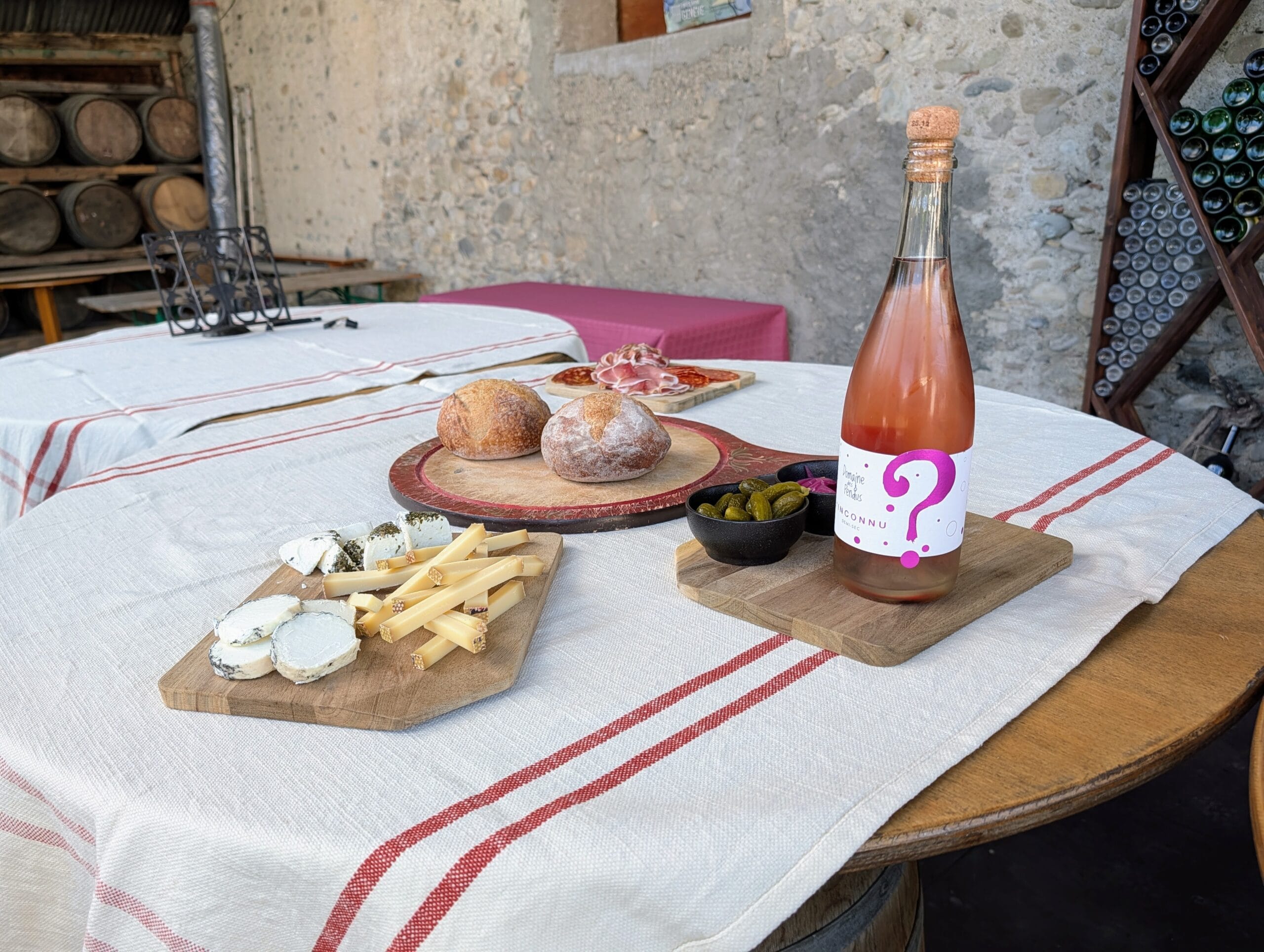 Een gedekte tafel met een fles roséwijn, diverse kazen, brood, charcuterie en augurken in een rustieke wijnkelder
