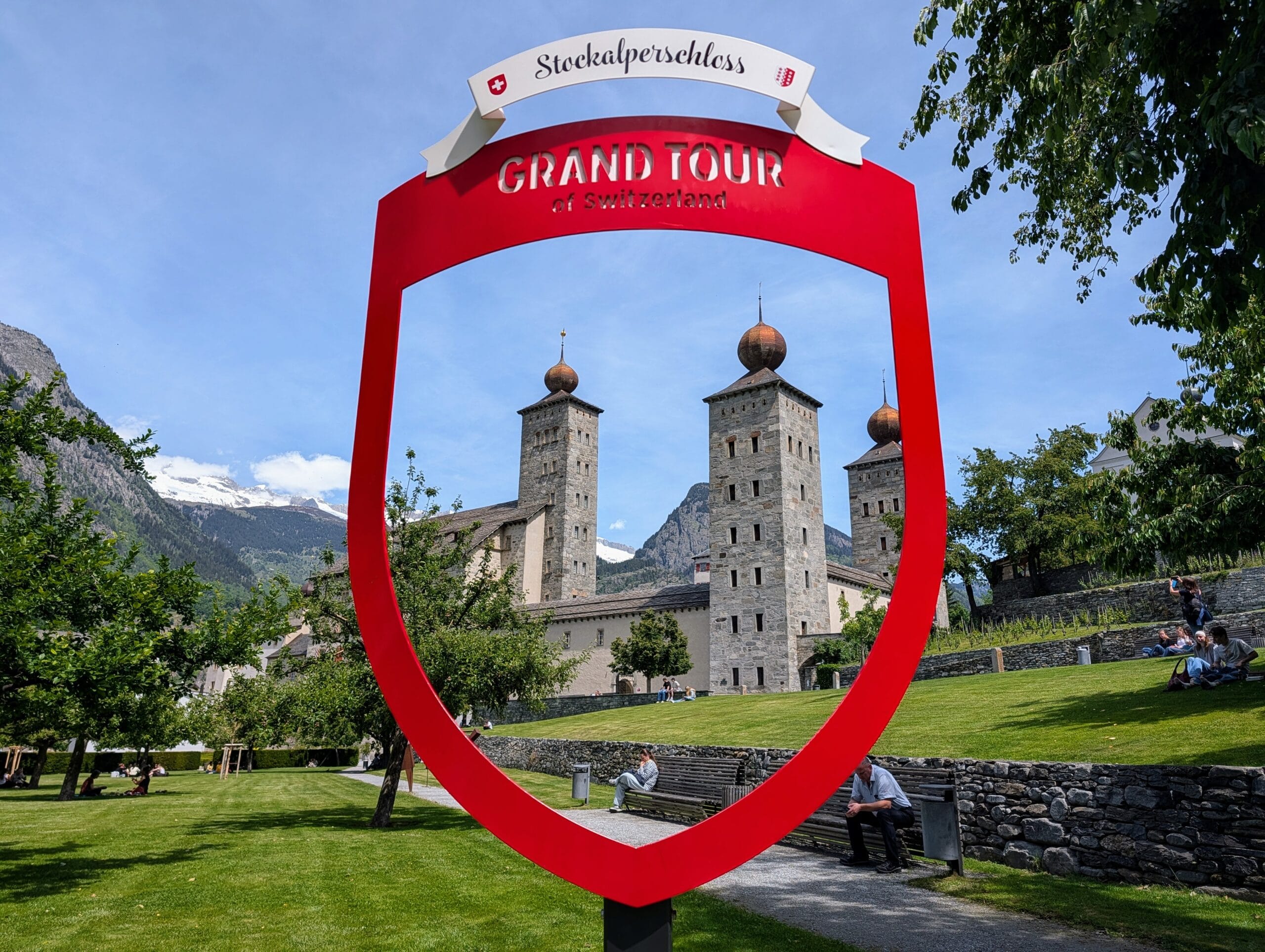 Het Stockalperschloss in Brig, omlijst door een rood Grand Tour of Switzerland-fotopunt met bergen op de achtergrond