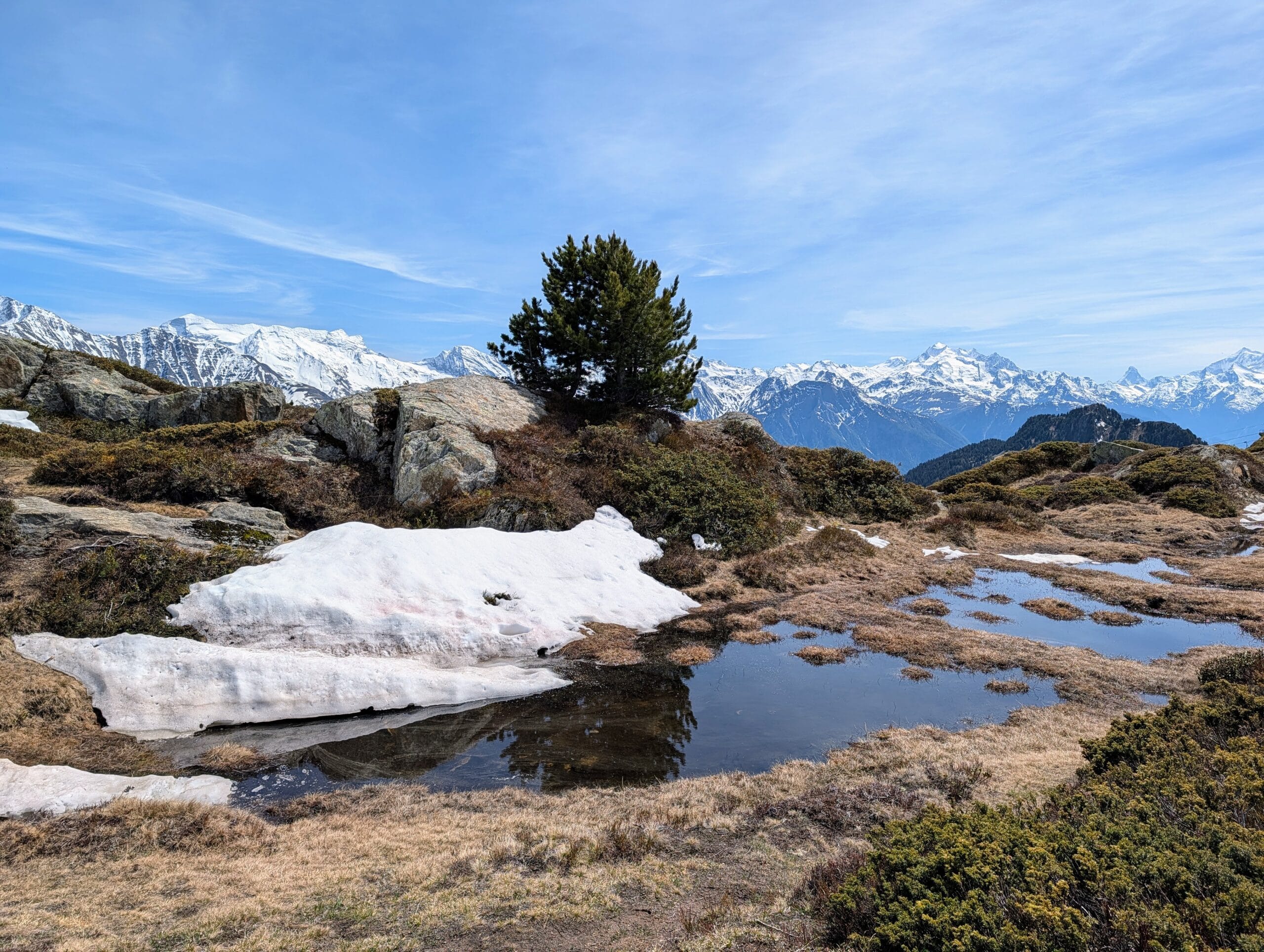 Alpenlandschap met smeltende sneeuw bij een bergmeertje en besneeuwde bergtoppen op de achtergrond