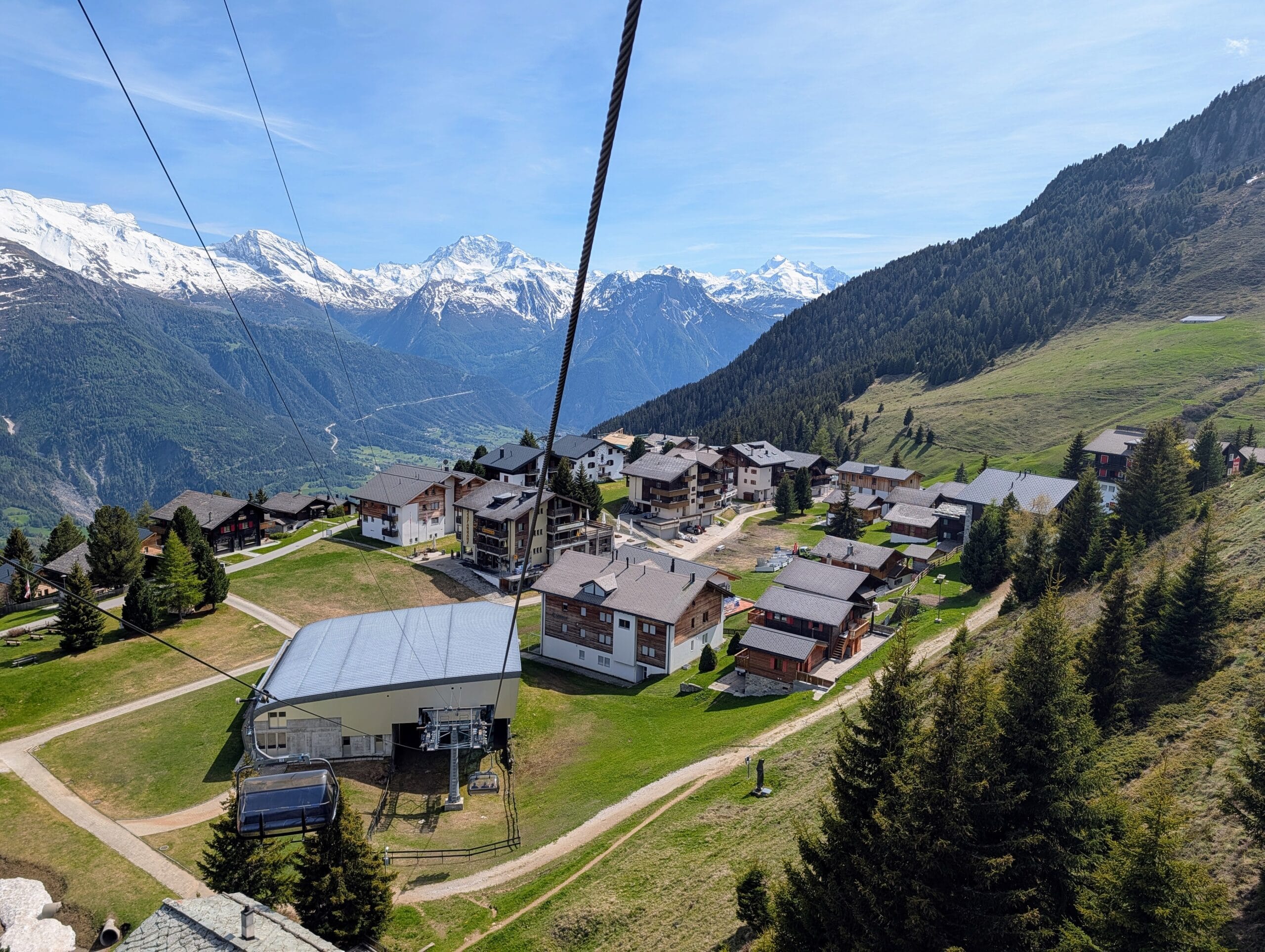 Uitzicht vanuit een kabelbaan op een bergdorpje in de Alpen met besneeuwde bergtoppen op de achtergrond