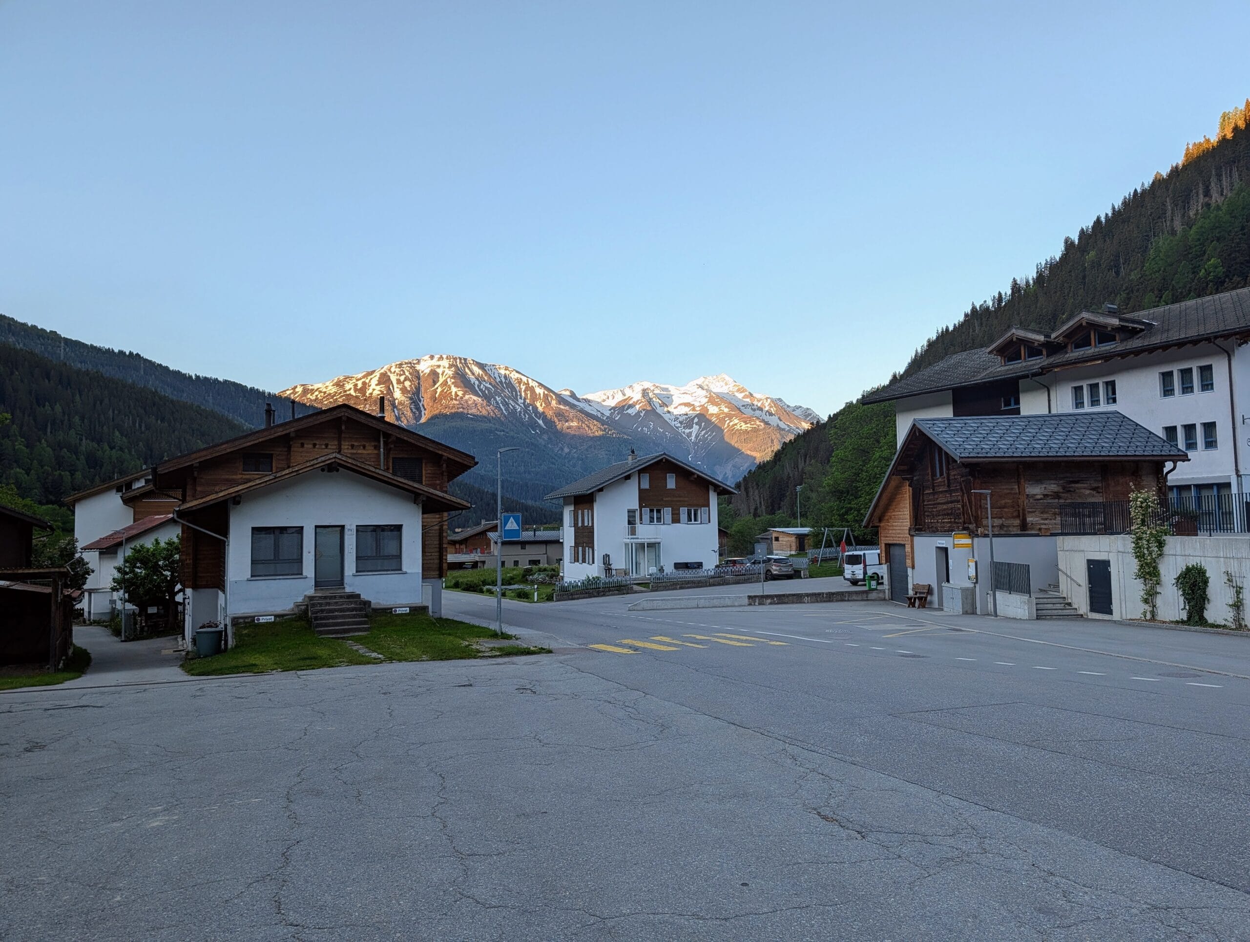 Berghuizen in een Alpenvallei met op de achtergrond besneeuwde bergtoppen die worden verlicht door de ondergaande zon