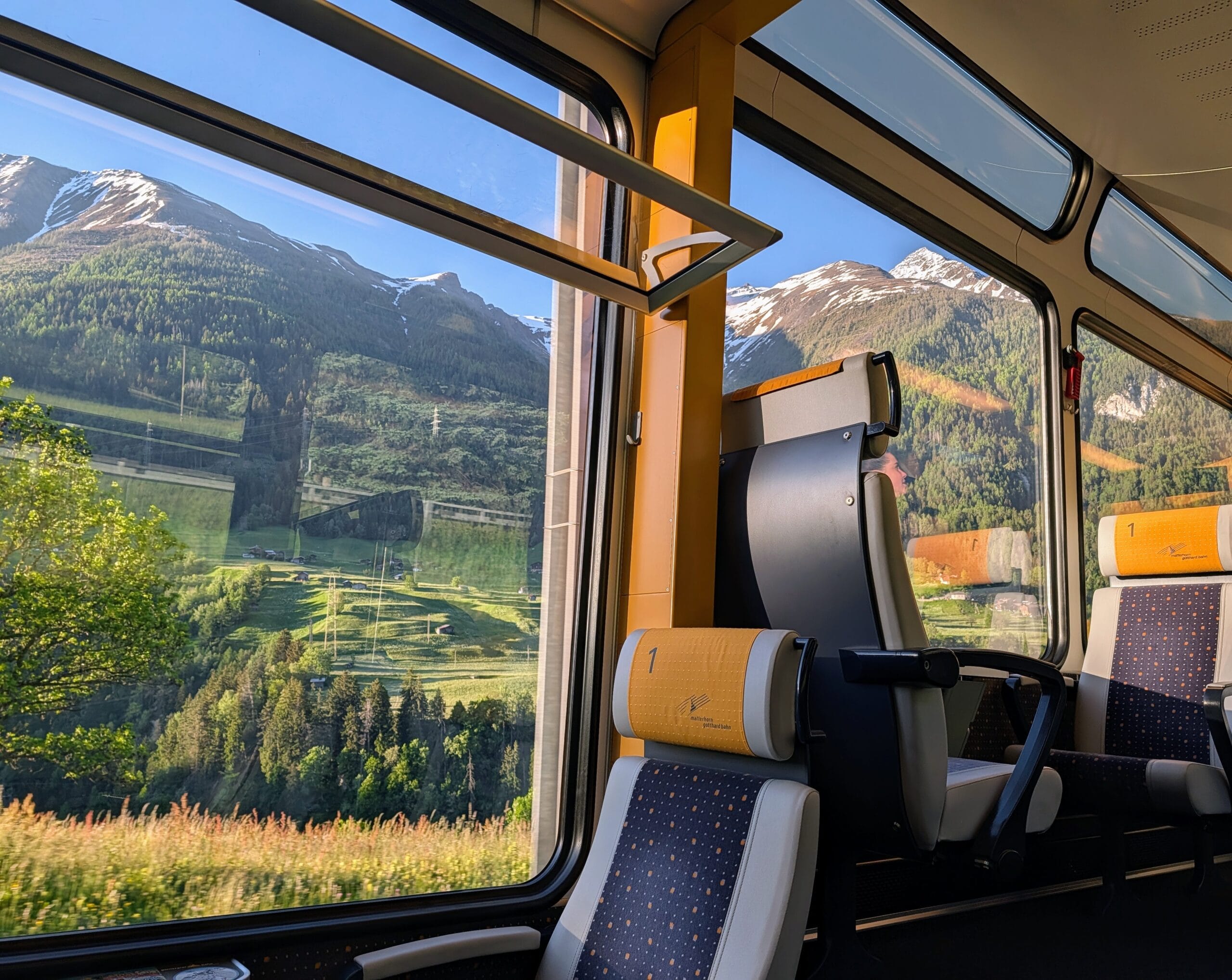 Uitzicht op groene bergen met besneeuwde toppen vanuit een panoramische treinwagon in Zwitserland