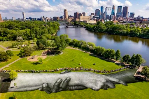 Luchtfoto van een gigantische muurschildering van in elkaar grijpende handen op het gras in een park in Minneapolis