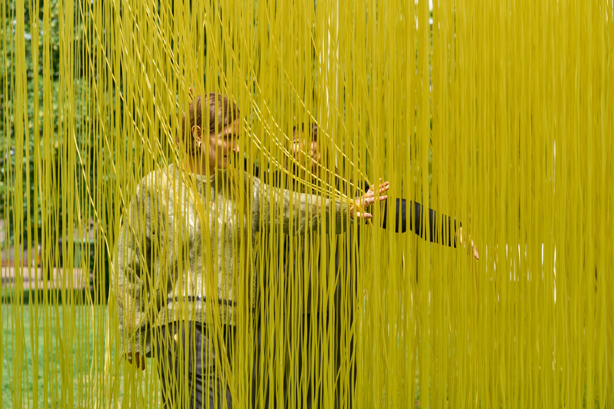 Een persoon loopt door een interactieve kunstinstallatie van dicht op elkaar hangende, verticale gele draden