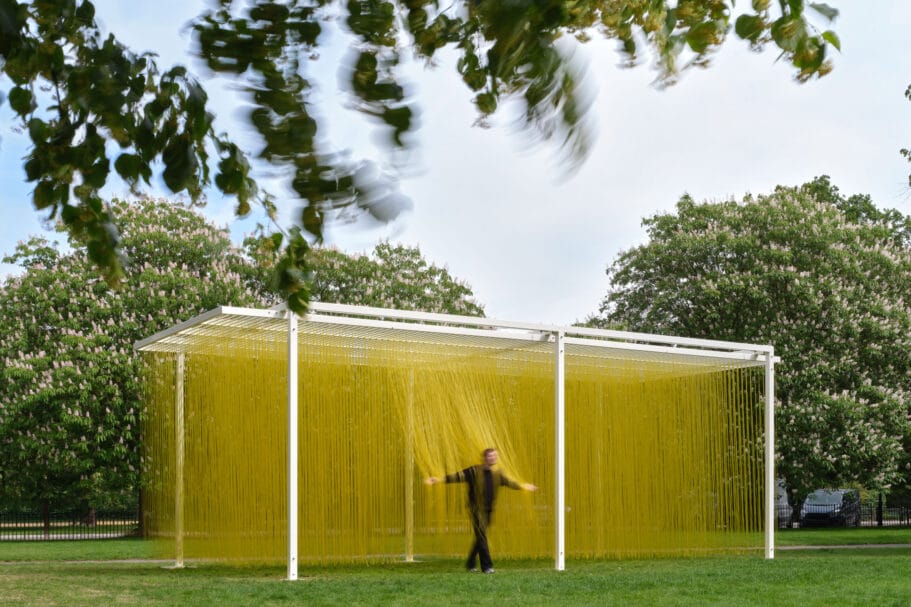 Een persoon loopt door een kunstinstallatie van duizenden hangende gele draden in een park