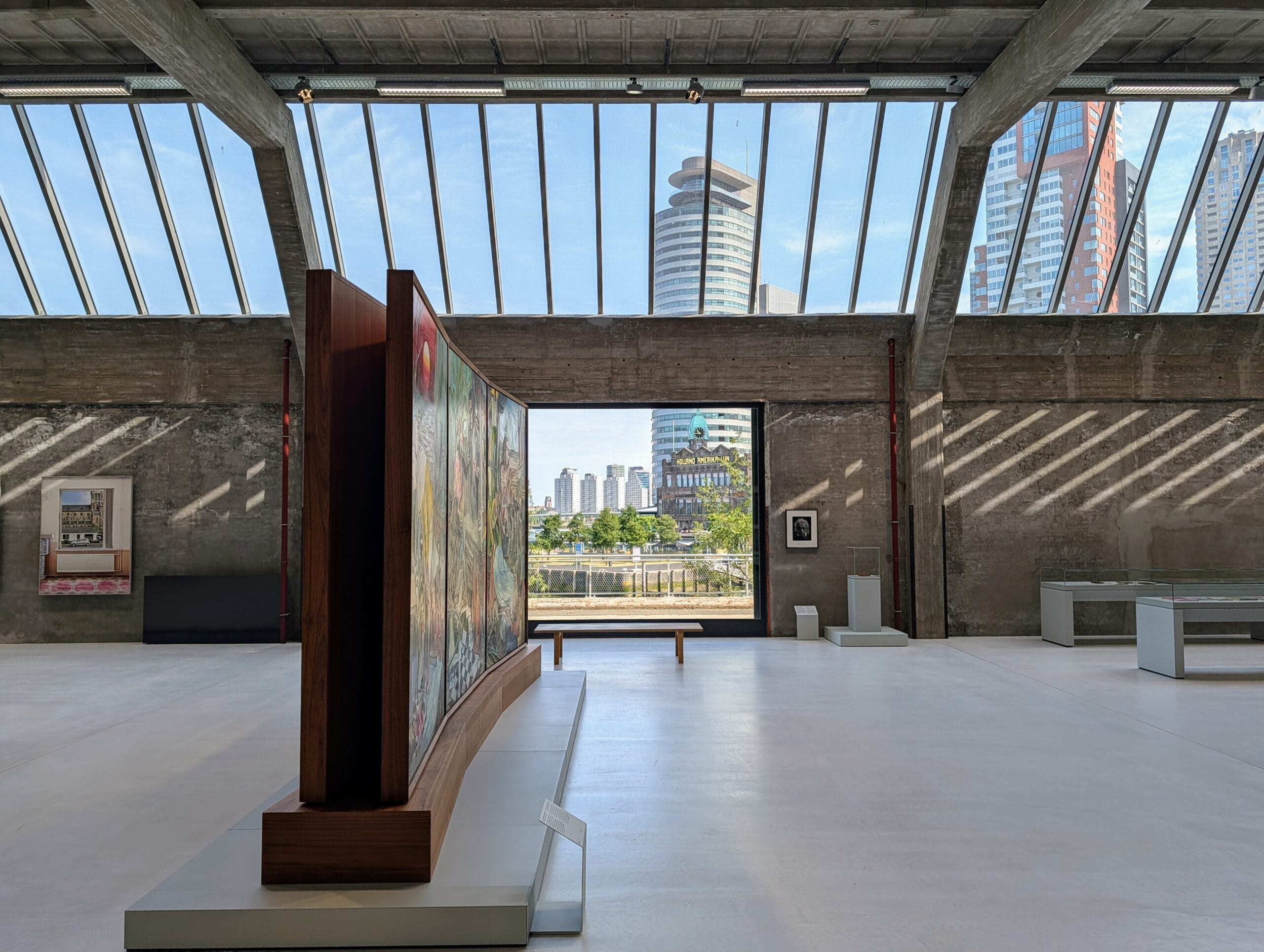 Een lichte museumzaal in Fenix Landverhuizersmuseum met uitzicht op Hotel New York en de skyline van Rotterdam