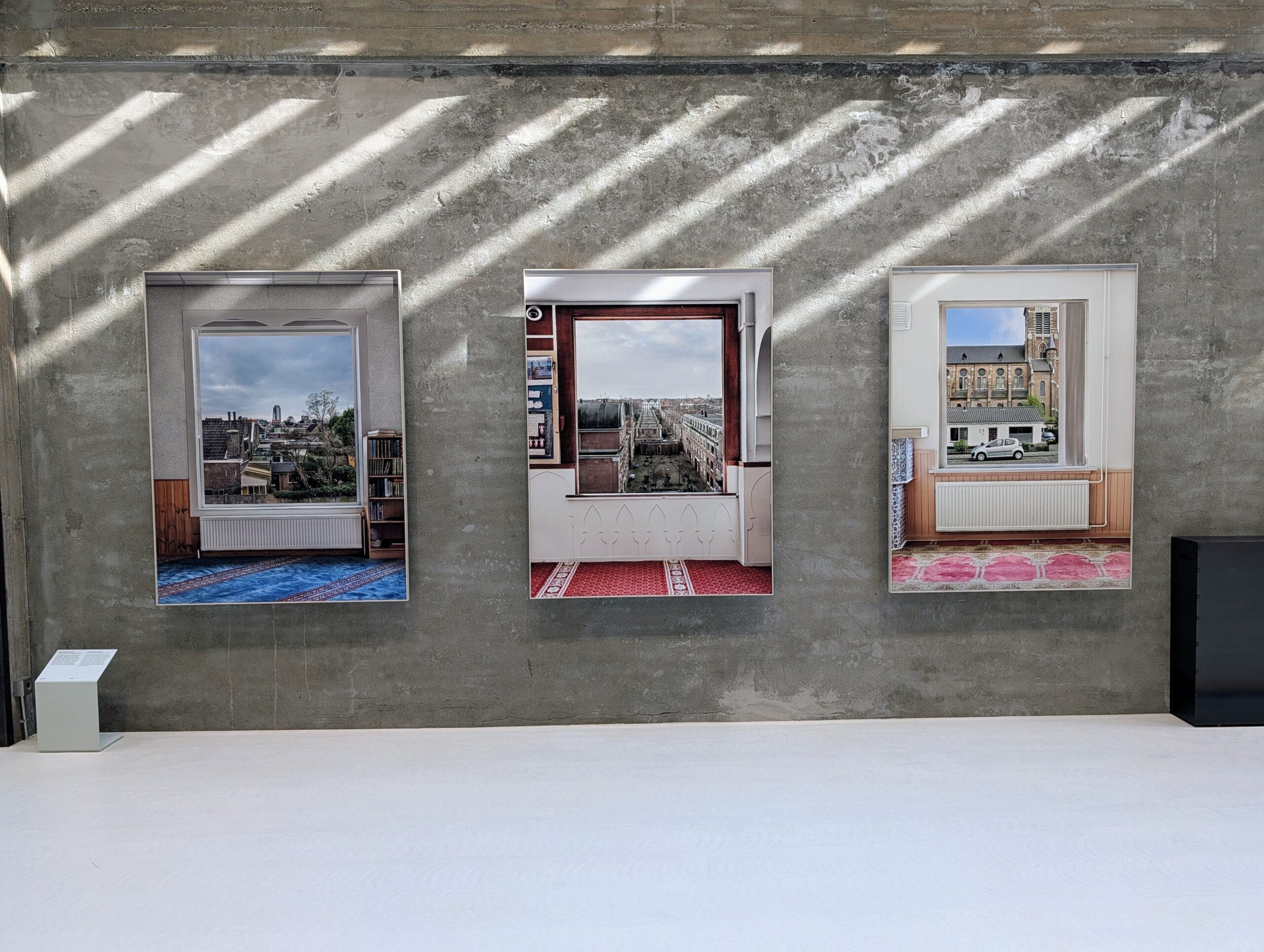 Drie ingelijste foto's van uitzichten vanuit moskeeën hangen naast elkaar op een betonnen muur in een museum