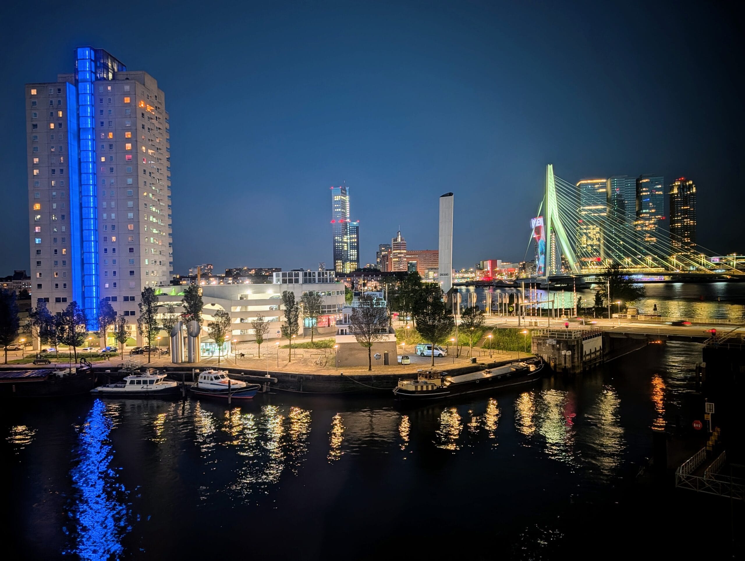 De skyline van Rotterdam bij nacht met de Erasmusbrug, verlichte wolkenkrabbers en reflecties op het water van de Maas