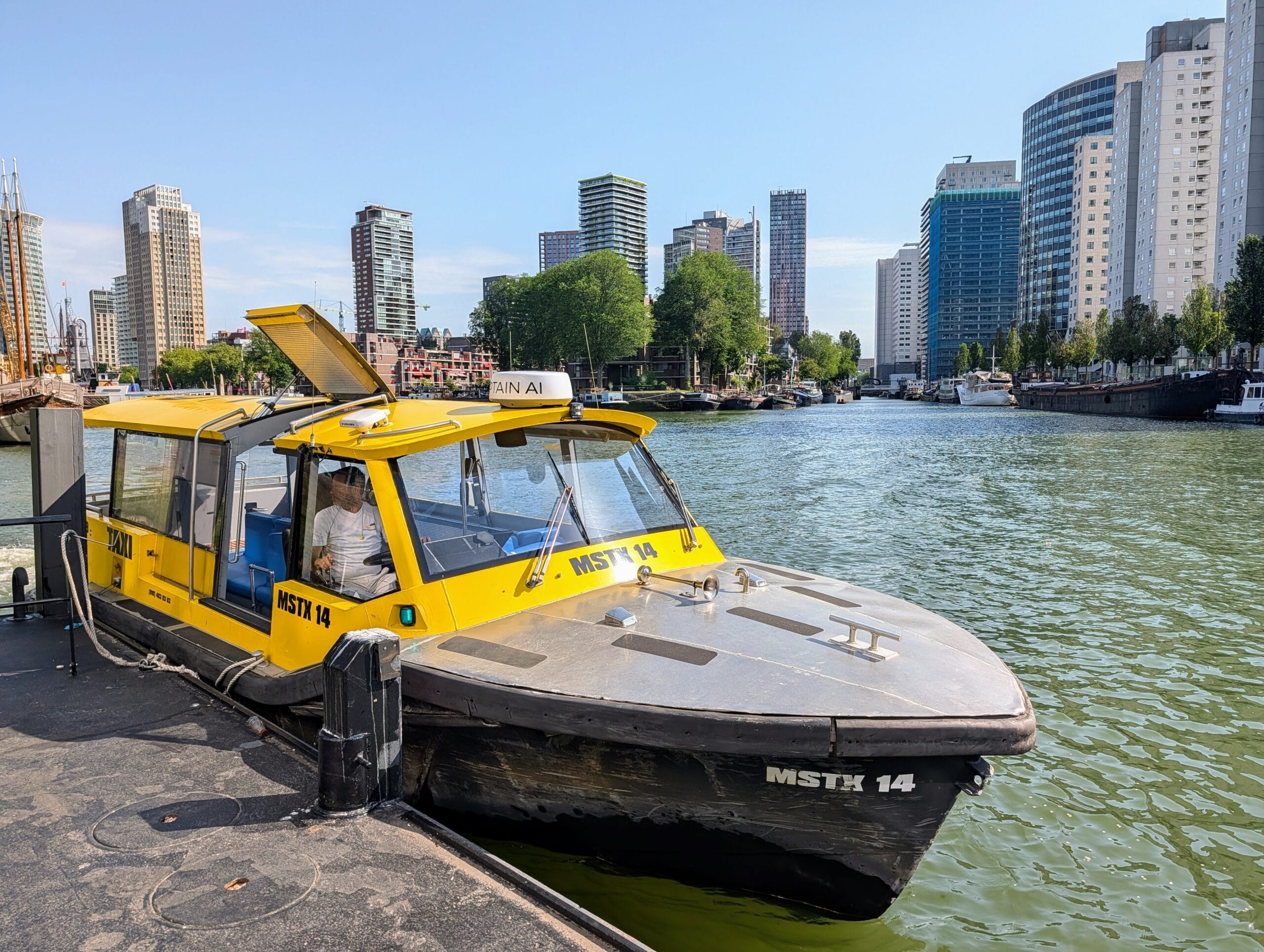 Een gele watertaxi ligt aangemeerd aan een kade in Rotterdam met op de achtergrond de skyline van de Kop van Zuid