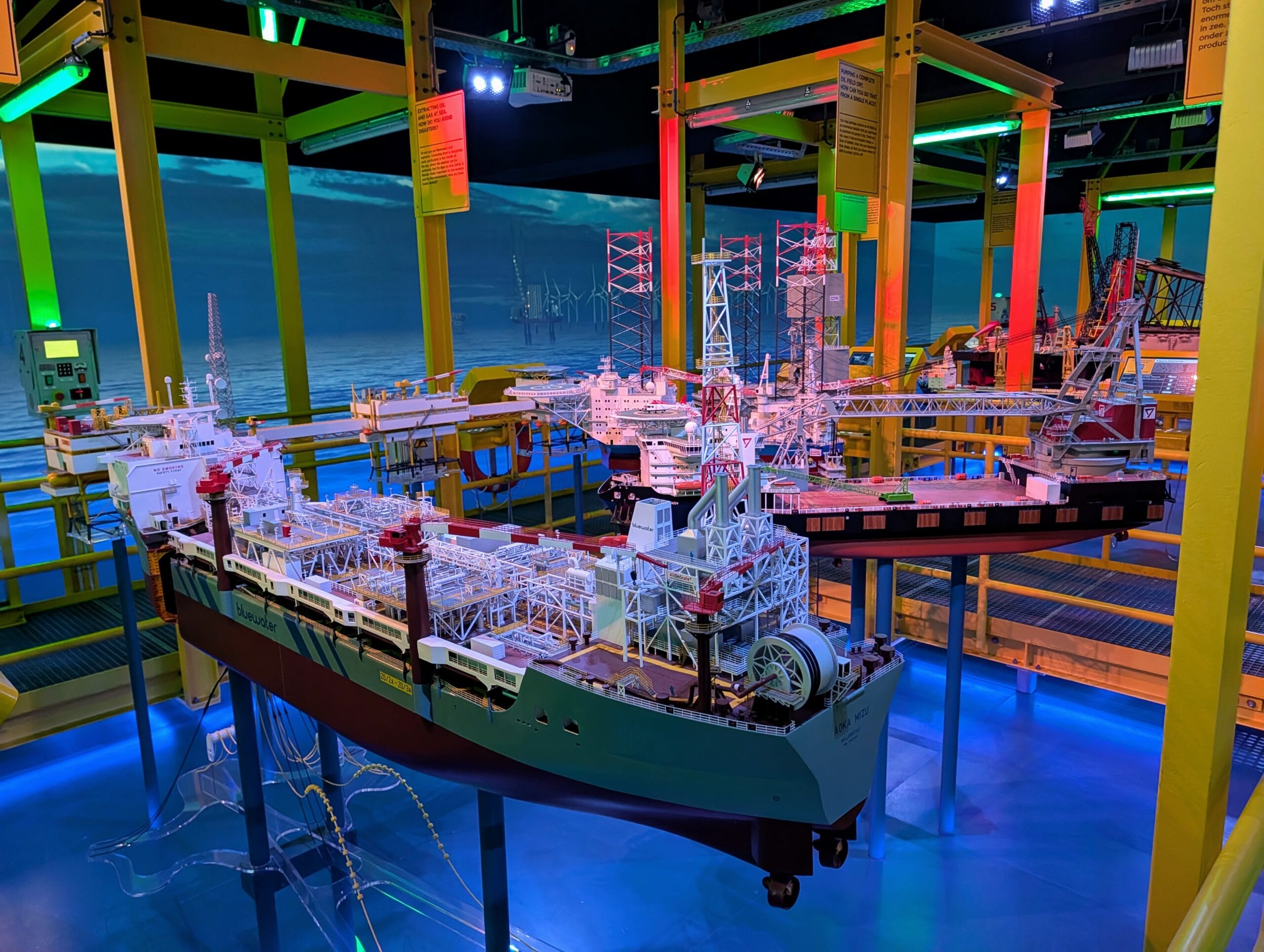 Gedetailleerde schaalmodellen van boorplatforms en offshore schepen in een museumopstelling met blauwe en gele verlichting