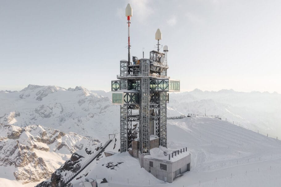 Een modern weerstation en zendmast met glazen uitkijkplatforms op een besneeuwde bergtop in de Alpen