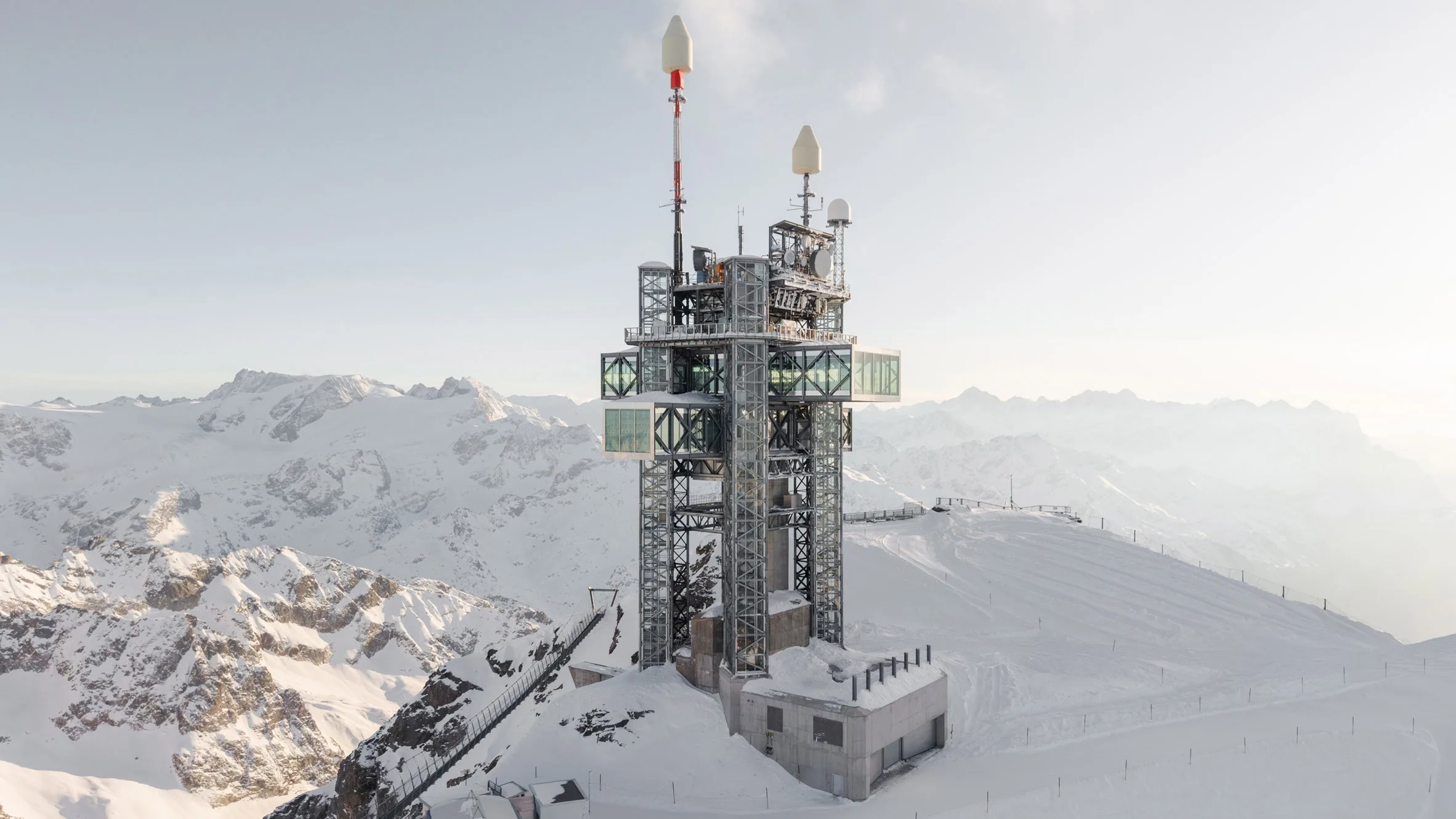 Een modern weerstation en zendmast met glazen uitkijkplatforms op een besneeuwde bergtop in de Alpen
