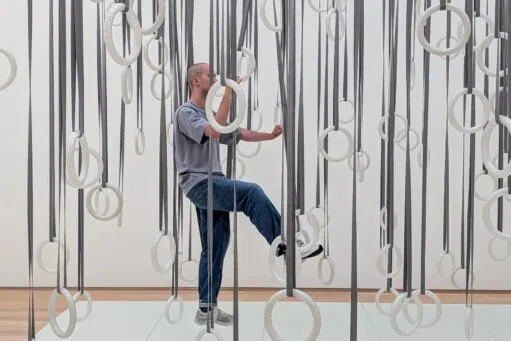 Een persoon stapt door een kunstinstallatie van talloze witte ringen die aan grijze linten van het plafond hangen